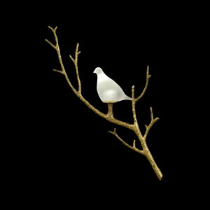 A decorative wall hanging featuring a small white bird perched on a bare gold branch, shown against a solid black background.